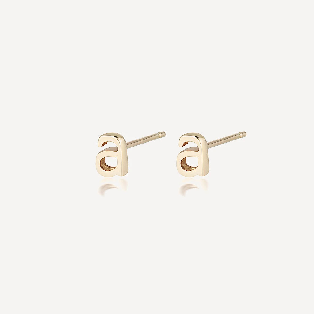Gold and silver letter a stud earrings with polished finish on a soft beige background, minimalist luxury jewelry product image.