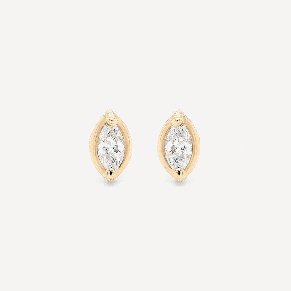 Gold marquise diamond stud earrings featuring brilliant marquise-cut stones in a polished gold setting on a soft beige background.