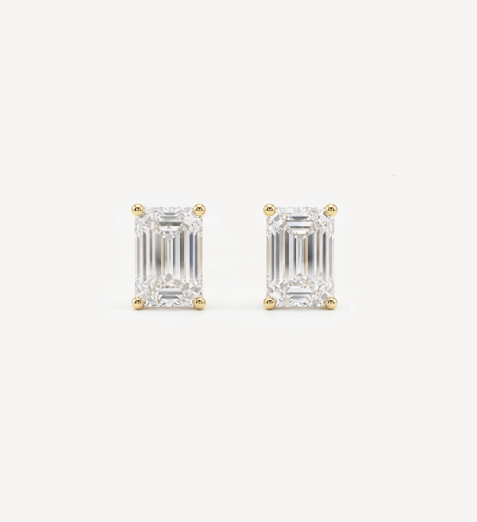 Large Emerald Grace diamond stud earrings in yellow gold featuring emerald-cut diamonds in classic four-prong settings, displayed as a matching pair