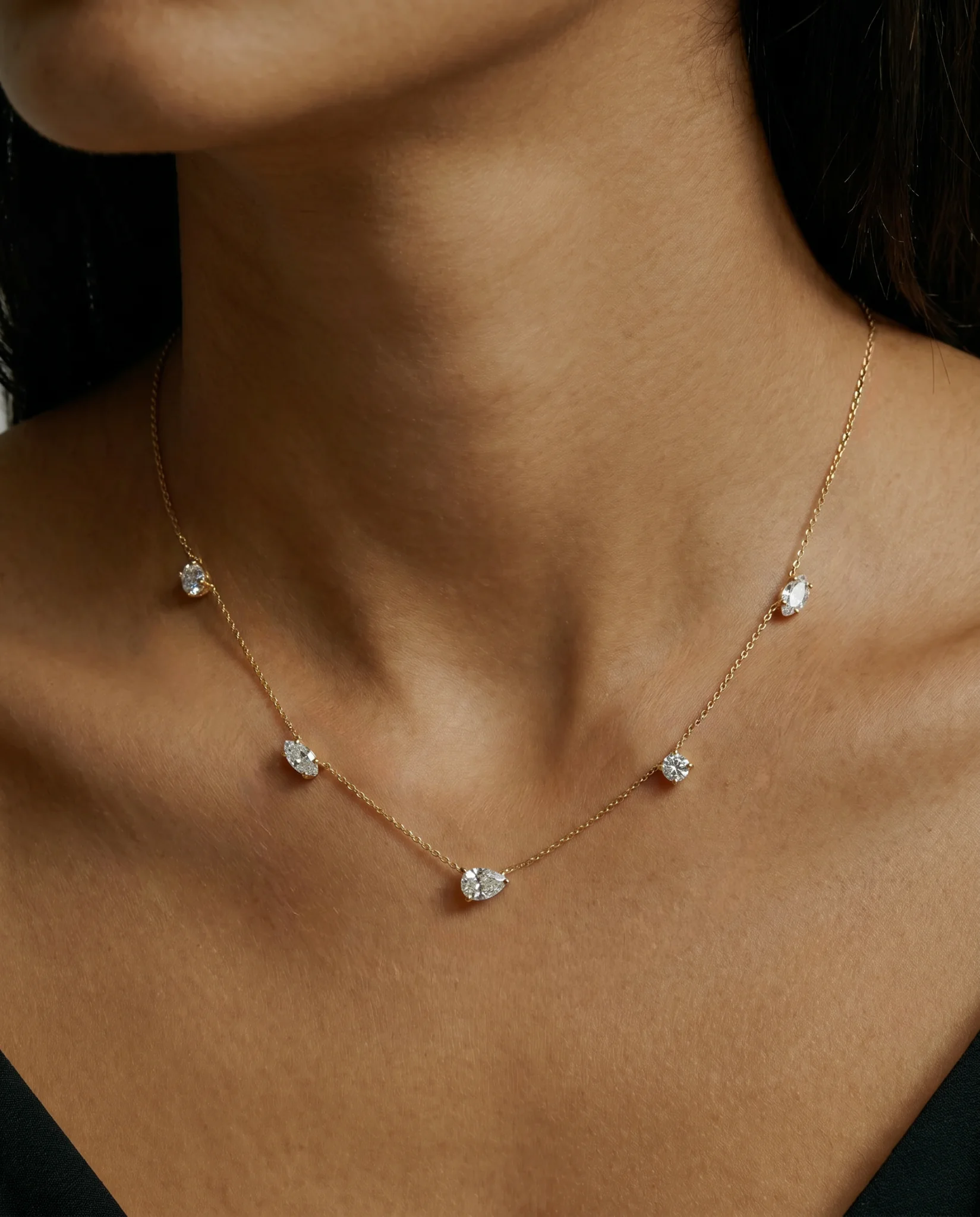 Nola Diamond Satellite Necklace by HLSK Jewellery in yellow gold featuring a pear-cut centre diamond and satellite-set diamonds on a fine chain, worn on a model in an angled close-up view.