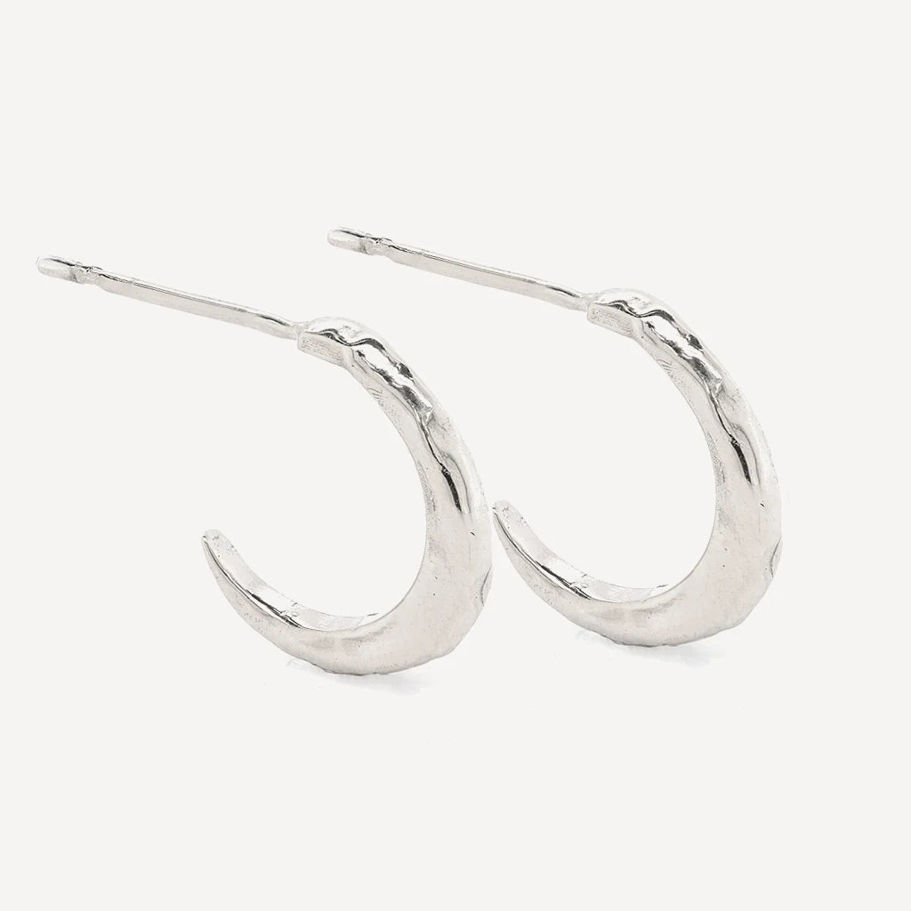 Silver crescent hoop stud earrings with a textured organic finish in polished sterling silver on a soft beige background.