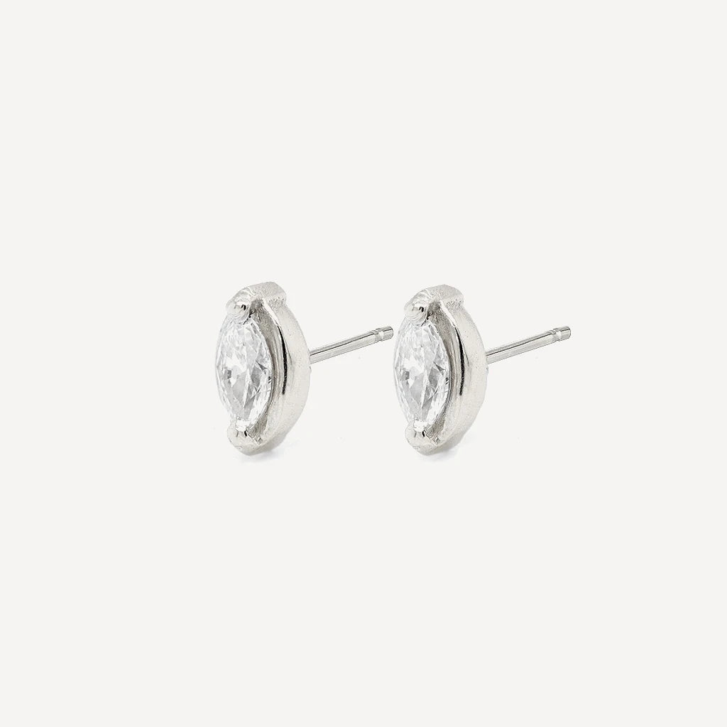 Side view of silver marquise diamond stud earrings with sparkling marquise-cut stones in a polished sterling silver setting on a soft beige background.