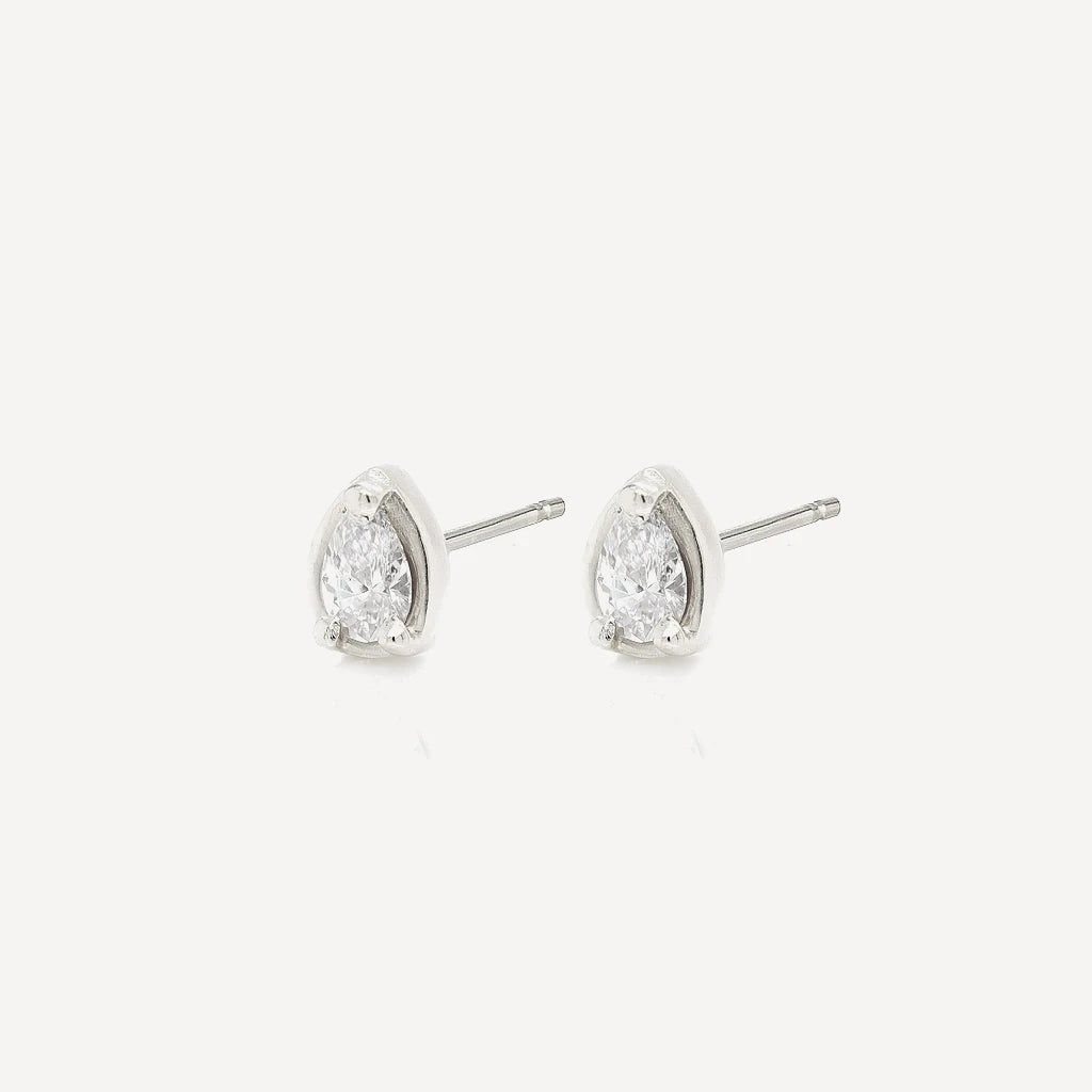Side view of silver petite pear diamond stud earrings with sparkling pear-cut stones in a polished sterling silver setting on a soft beige background.