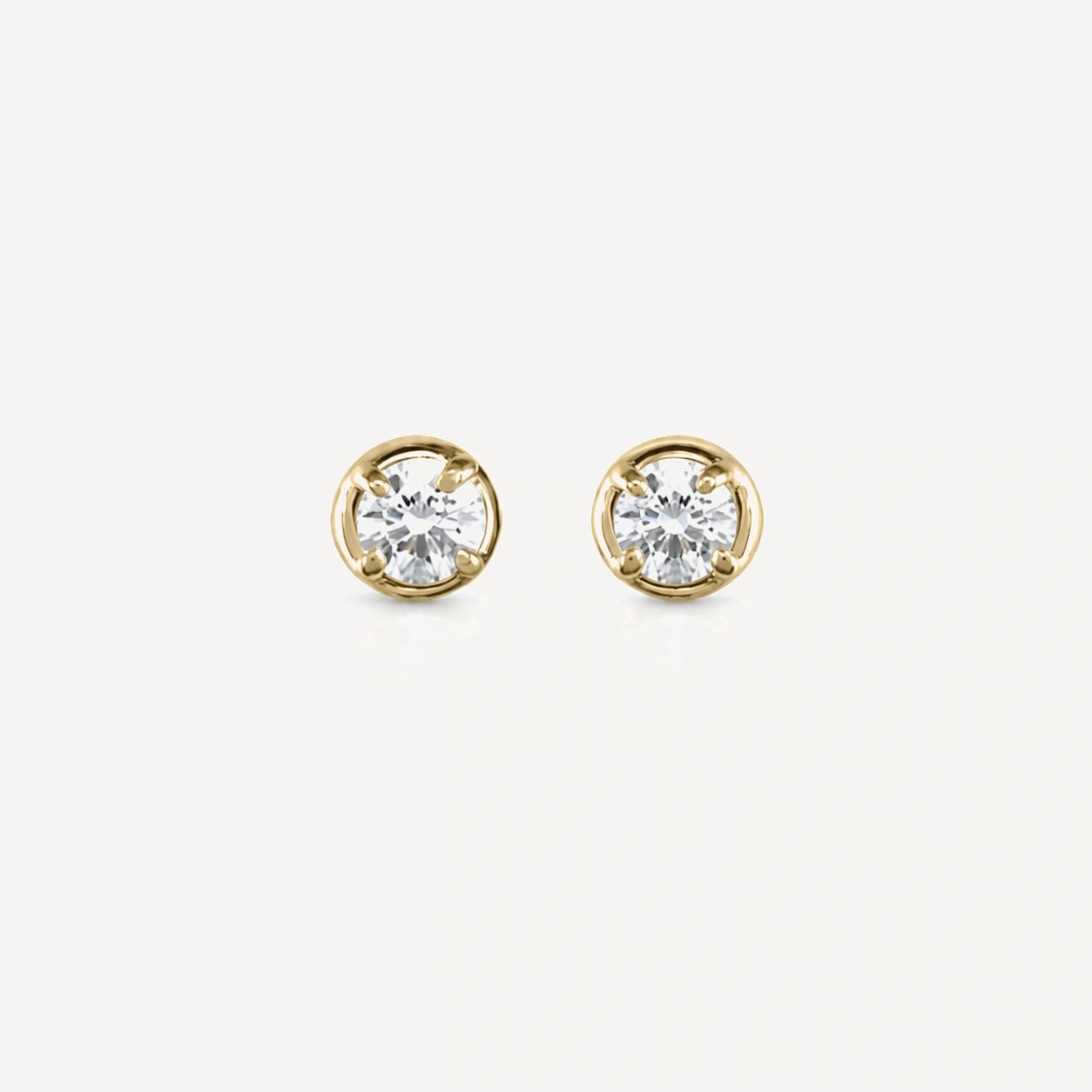 Yellow gold bezel-set diamond stud earrings featuring brilliant-cut round diamonds in a timeless minimalist design on a soft beige background.