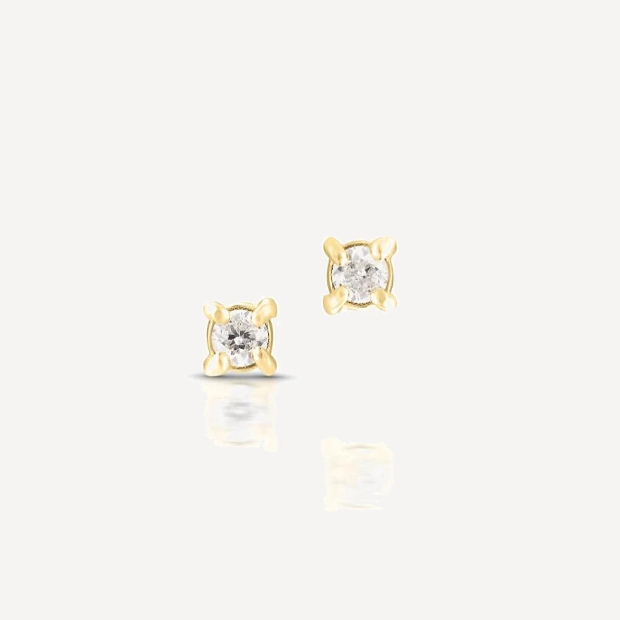 Yellow gold single diamond stud earrings featuring brilliant-cut diamonds in a classic four-prong setting on a soft beige background.