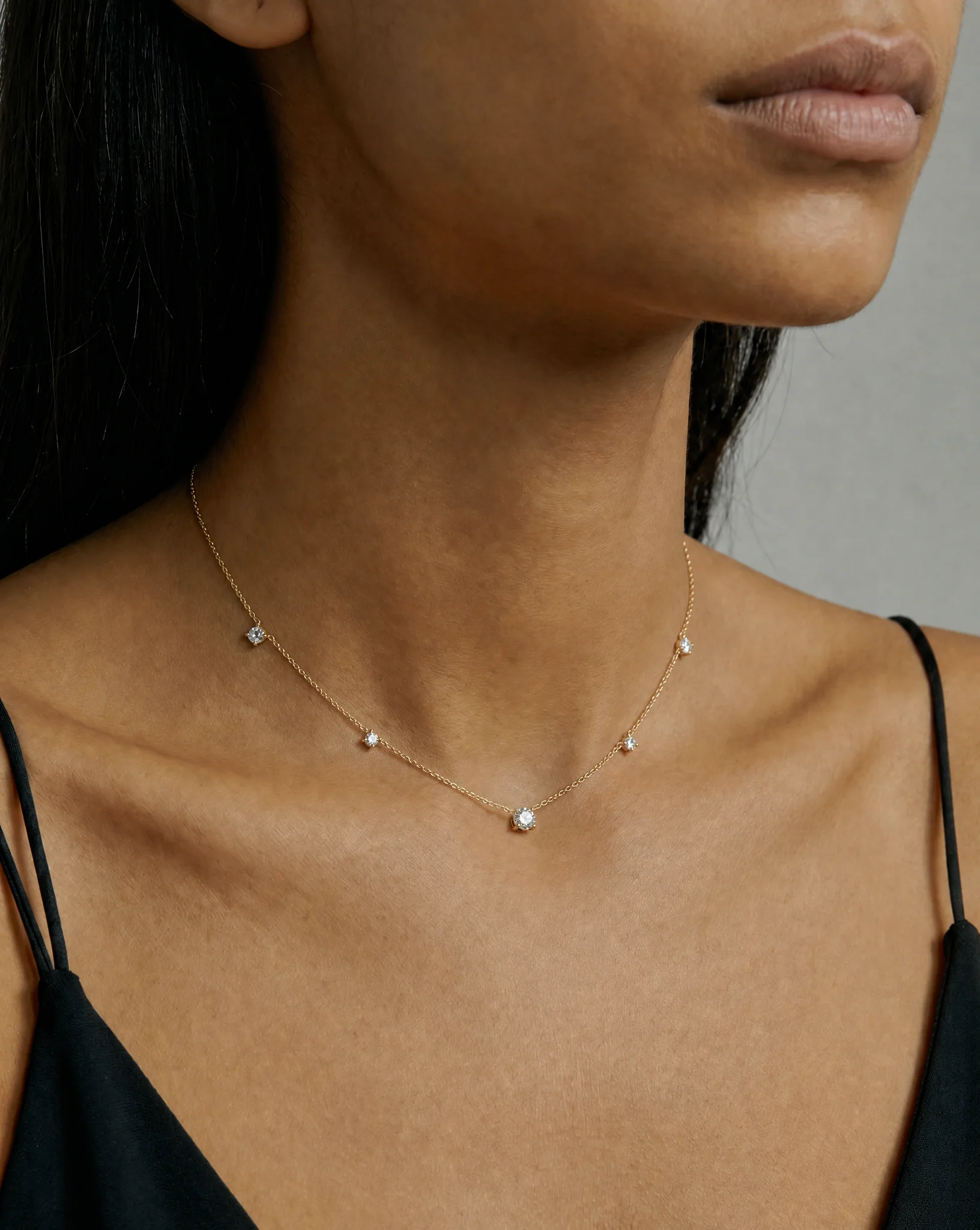 Celeste Satellite Necklace in yellow gold featuring a central round stone and four satellite-set stones on a delicate fine chain, worn on a model in an angled portrait view.