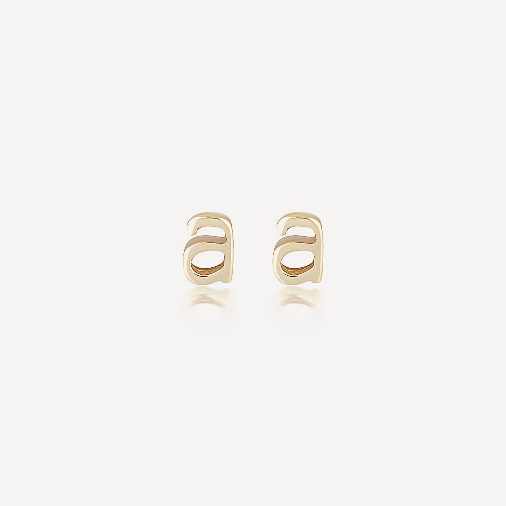 Gold lowercase letter A stud earrings in polished yellow gold on a soft neutral background.