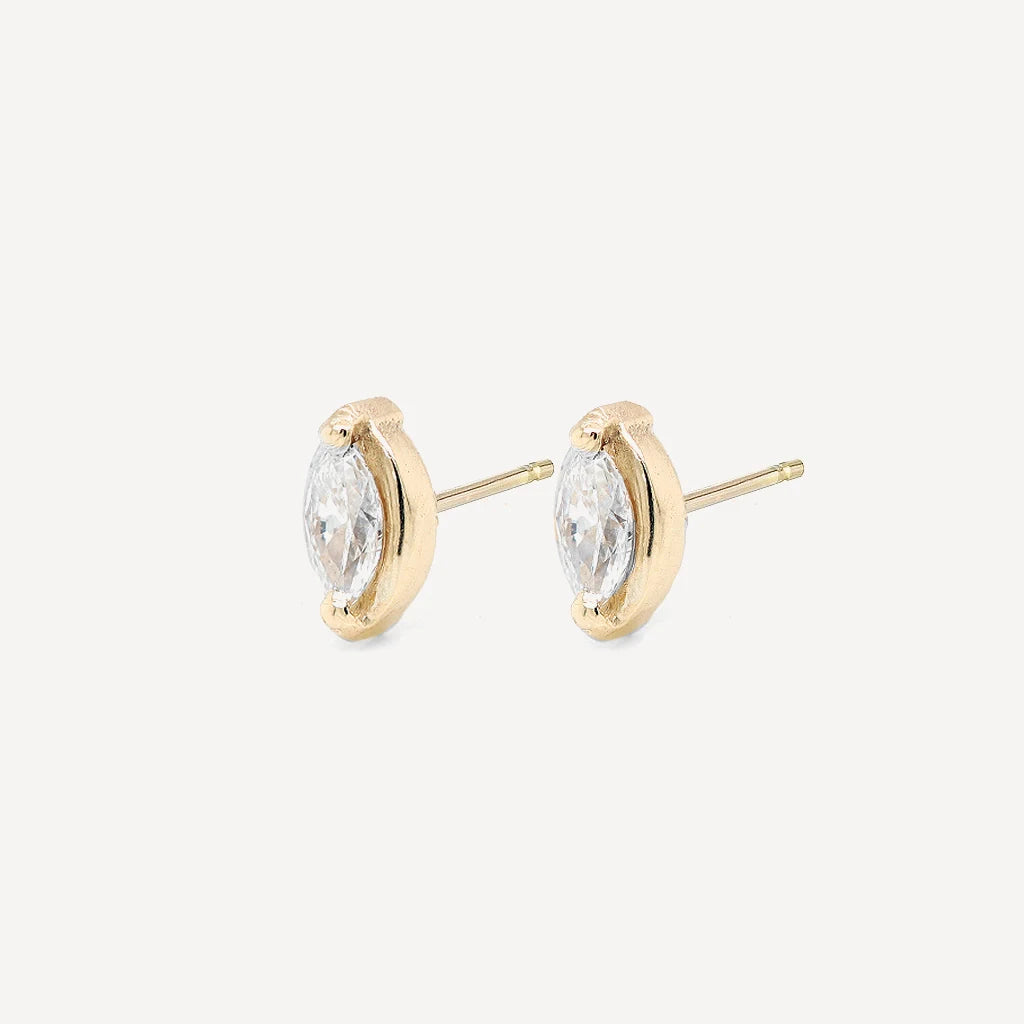 Side view of gold marquise diamond stud earrings with sparkling marquise-cut stones in a polished gold setting on a soft beige background.