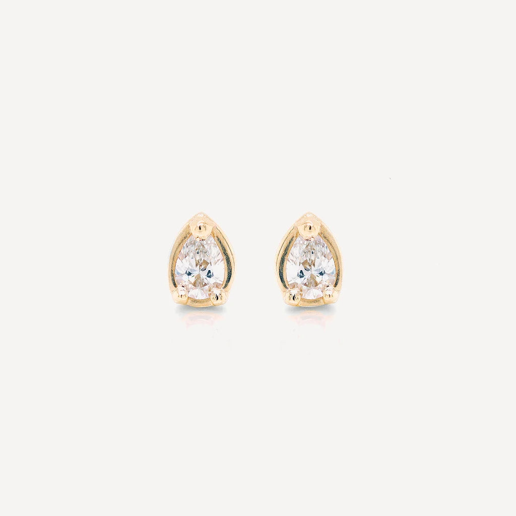 Gold petite pear diamond stud earrings featuring brilliant pear-cut stones in a polished gold setting on a soft beige background.