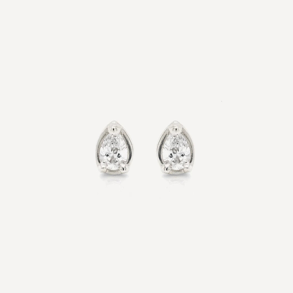 Silver petite pear diamond stud earrings featuring brilliant pear-cut stones in a polished sterling silver setting on a soft beige background.