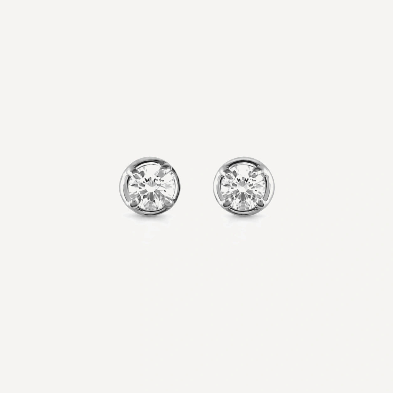 Sterling silver bezel-set diamond stud earrings featuring brilliant-cut round diamonds in a minimalist everyday design on a soft beige background.