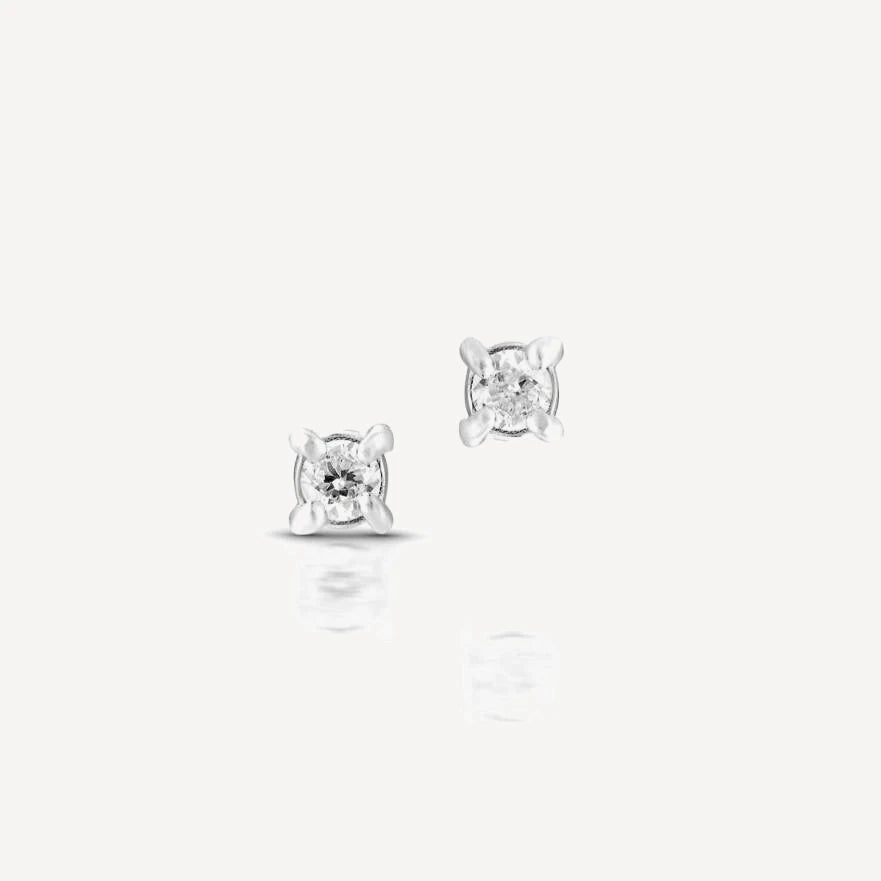 Sterling silver single diamond stud earrings featuring brilliant-cut diamonds in a classic four-prong setting on a soft beige background.
